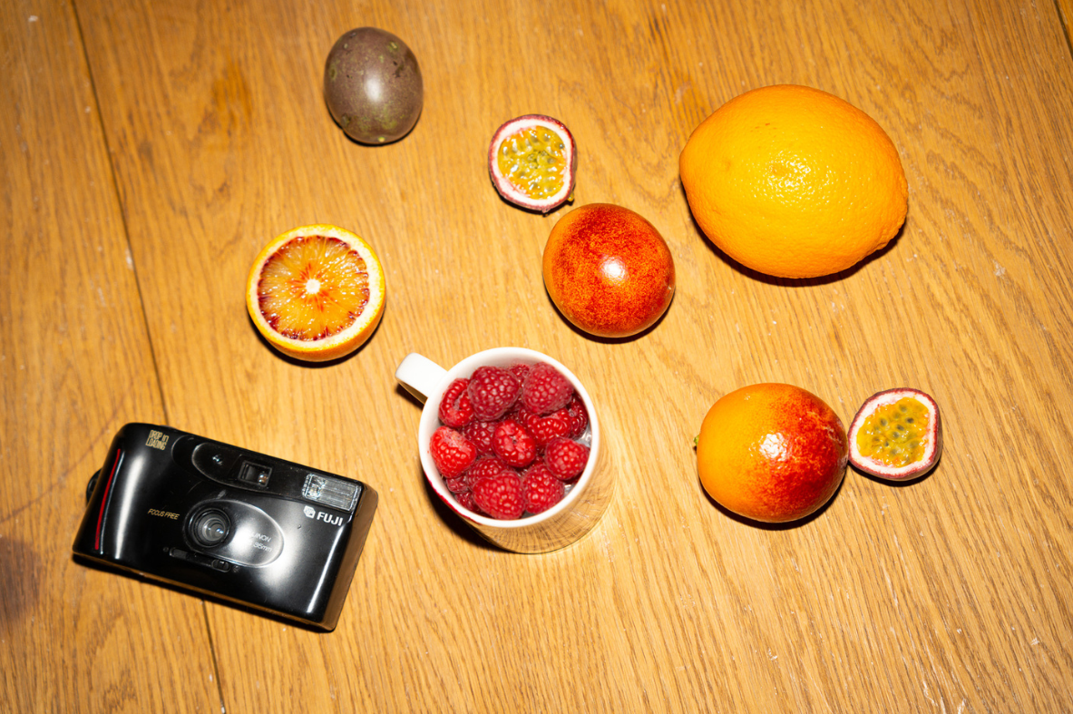 Hedelmiä ja Fuji-kamera pöydällä.